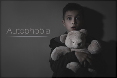 Image of Scared little with toy near dark wall. Autophobia - fear of isolation