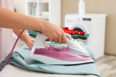 Young woman ironing clothes on board in bathroom, closeup