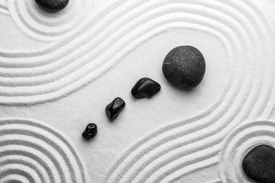 Photo of Black stones on sand with pattern, top view. Zen, meditation, harmony
