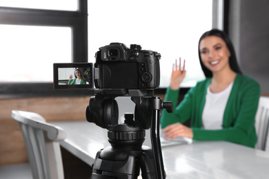 Young blogger with laptop recording video at cafe, focus on camera screen