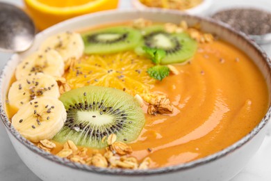 Photo of Bowl of delicious fruit smoothie with fresh banana, kiwi slices and granola served on white table, closeup