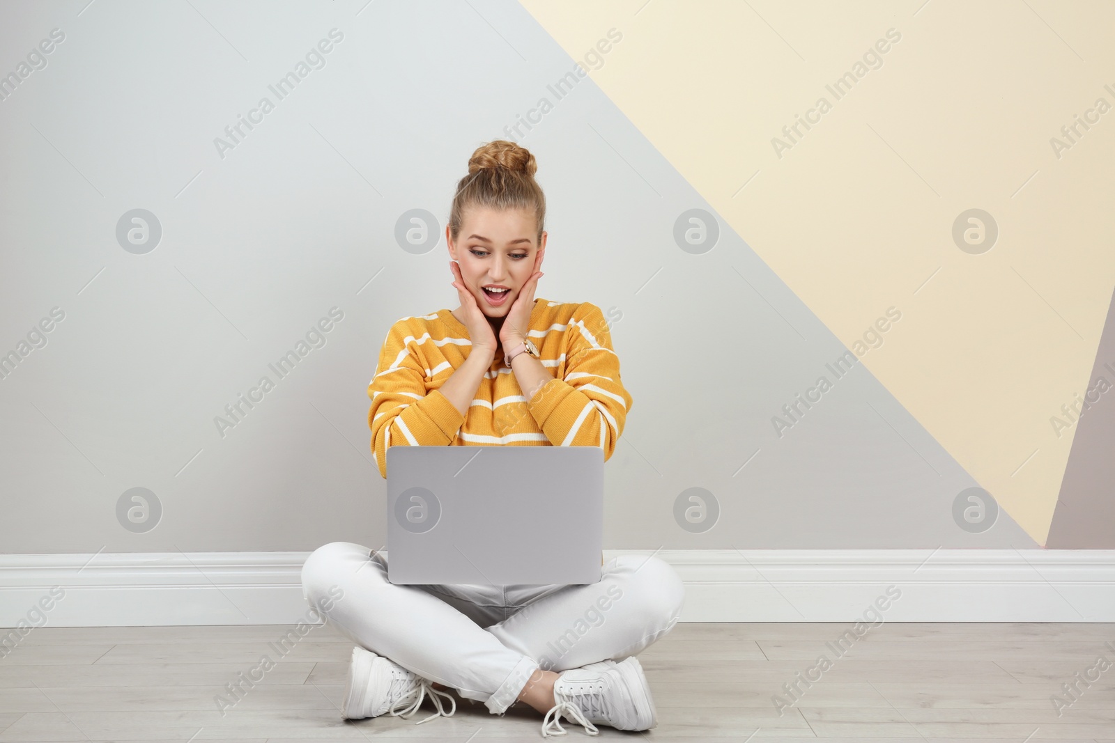 Photo of Emotional young woman with laptop on floor near color wall. Space for text