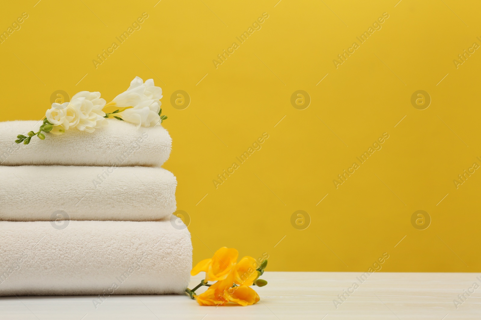 Photo of Stack of soft clean towels with beautiful flowers on table against color background. Space for text