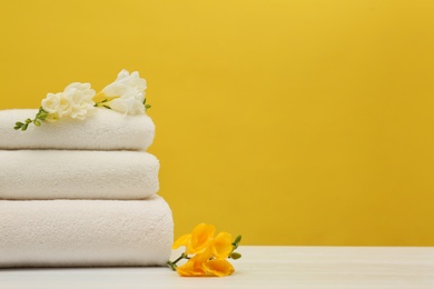 Stack of soft clean towels with beautiful flowers on table against color background. Space for text