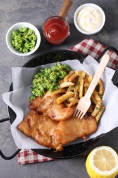 Photo of Tasty fish, chips, sauces and peas on grey table, flat lay