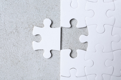 Photo of Blank white puzzle with separated piece on light grey stone background, flat lay