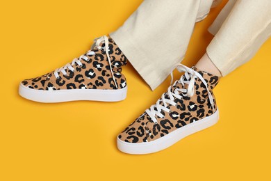 Photo of Woman wearing classic old school sneakers with leopard print on orange background, above view
