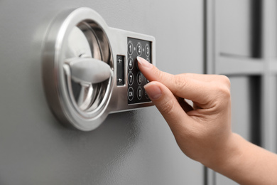 Photo of Woman entering code on keypad of modern safe, closeup