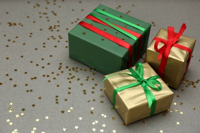 Photo of Christmas gift boxes and shiny confetti on grey background. Space for text