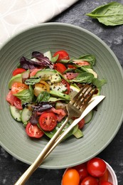 Photo of Delicious vegetable salad on black textured table, flat lay