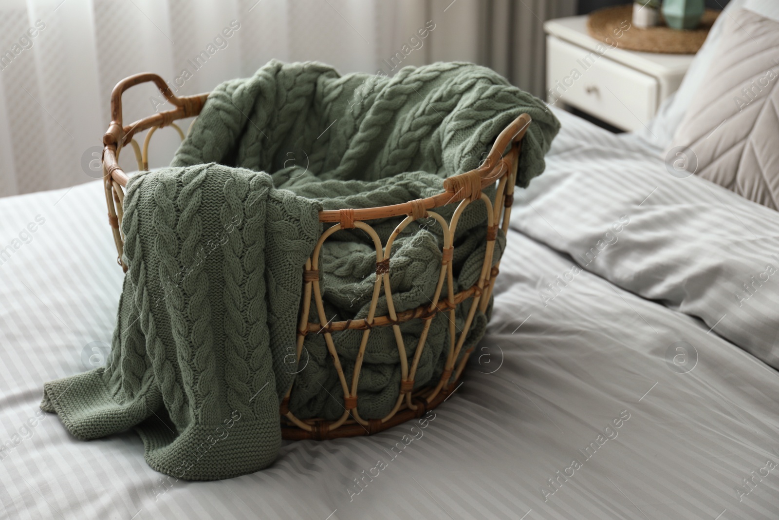 Photo of Knitted green plaid in wicker basket on bed indoors