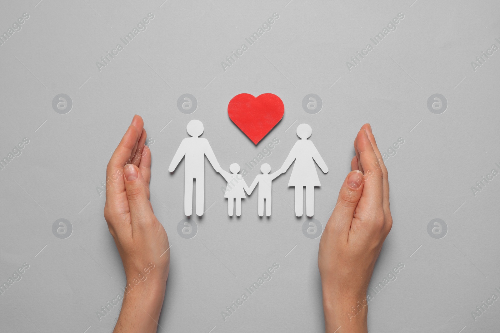 Photo of Woman protecting paper family cutout on grey background, top view. Insurance concept