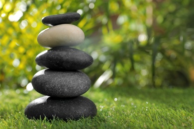 Photo of Stack of stones on green grass against blurred background, space for text. Zen concept