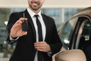 Photo of Young salesman with key near car in dealership, closeup