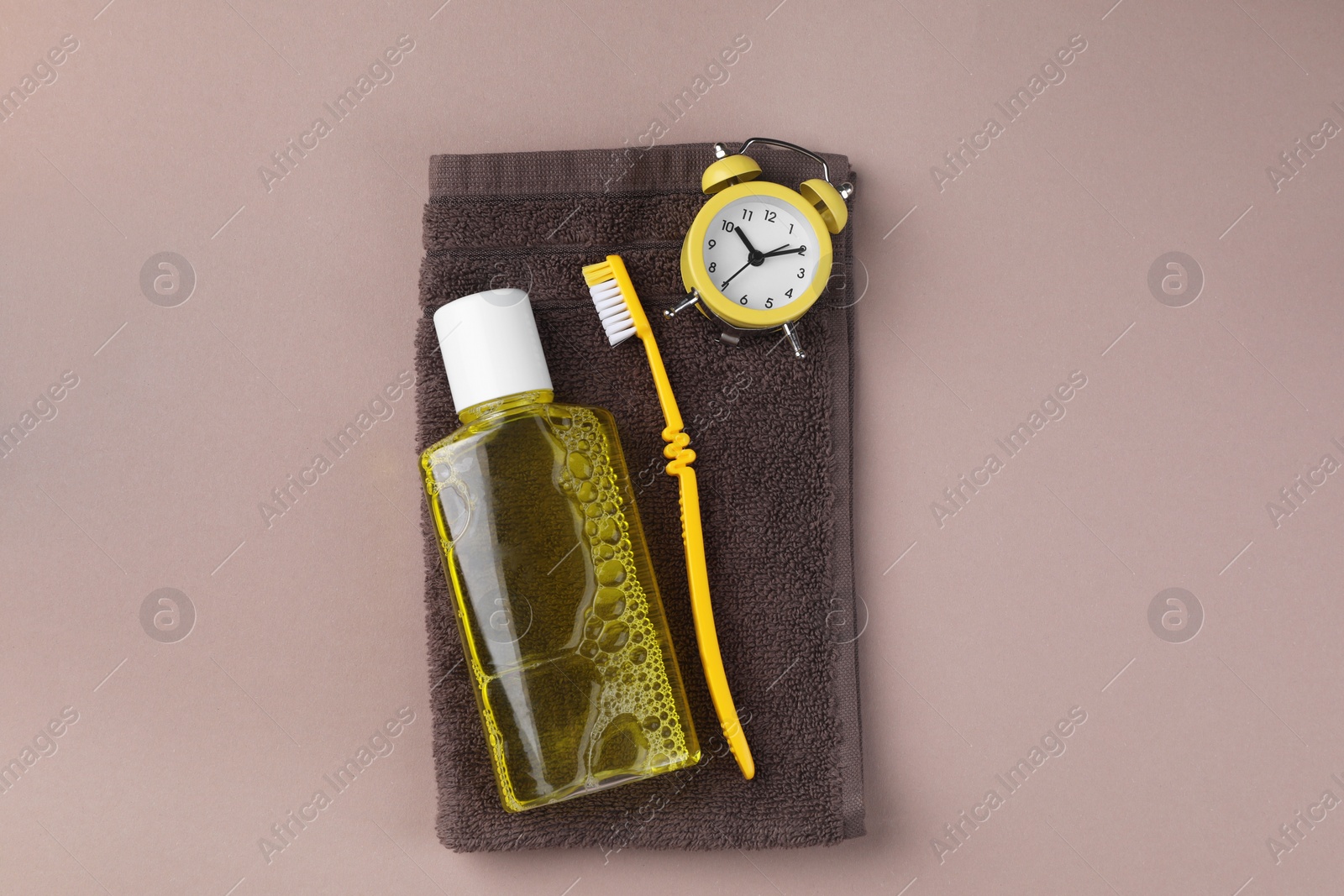 Photo of Fresh mouthwash in bottle, toothbrush, alarm clock and towel on beige background, top view