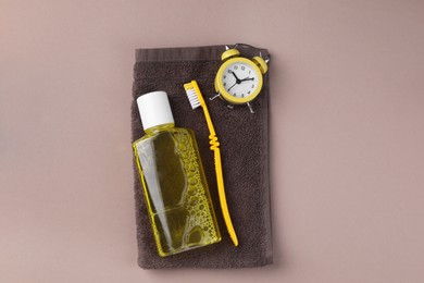 Photo of Fresh mouthwash in bottle, toothbrush, alarm clock and towel on beige background, top view