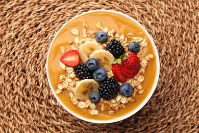 Photo of Delicious smoothie bowl with fresh berries, banana and oatmeal on woven mat, top view