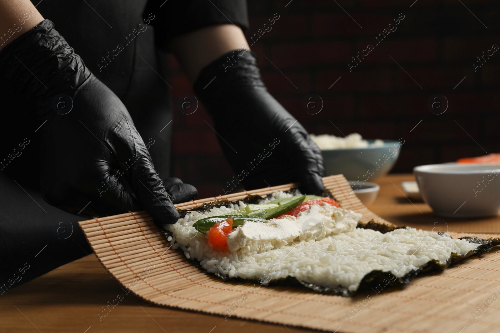 Photo of Chef in gloves making sushi roll at wooden table, closeup