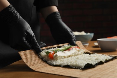 Photo of Chef in gloves making sushi roll at wooden table, closeup