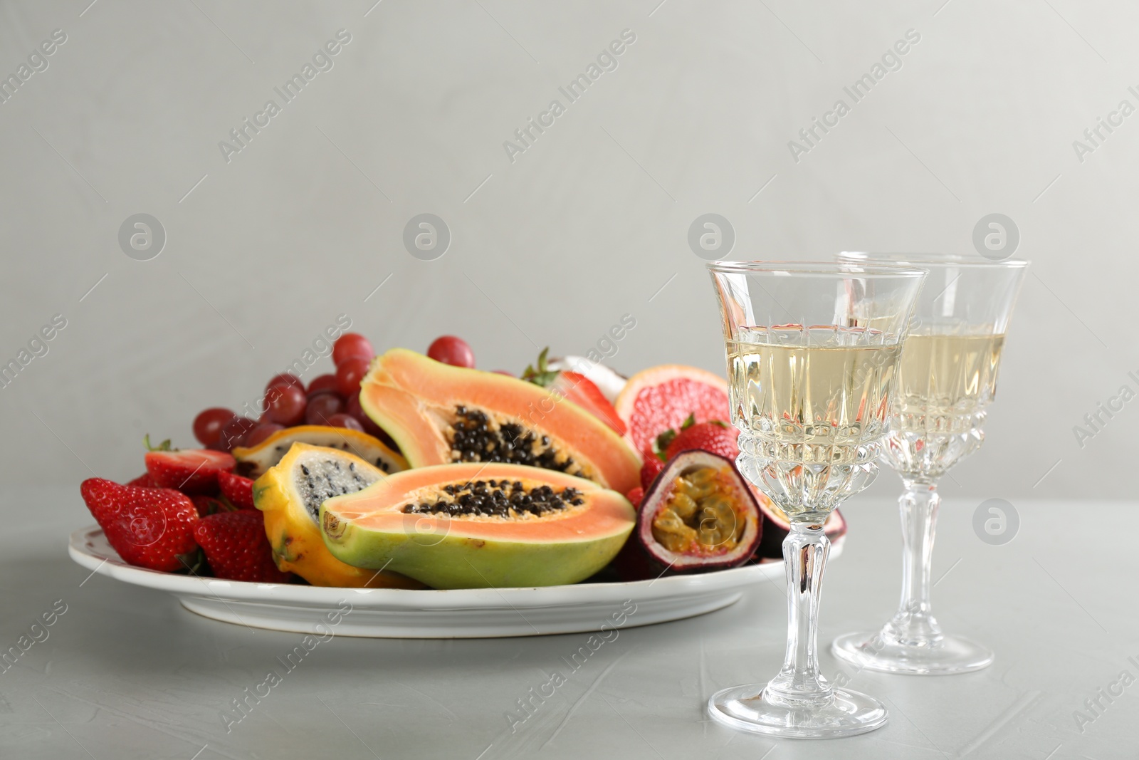 Photo of Delicious exotic fruits and glasses of wine on light grey table