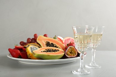 Delicious exotic fruits and glasses of wine on light grey table