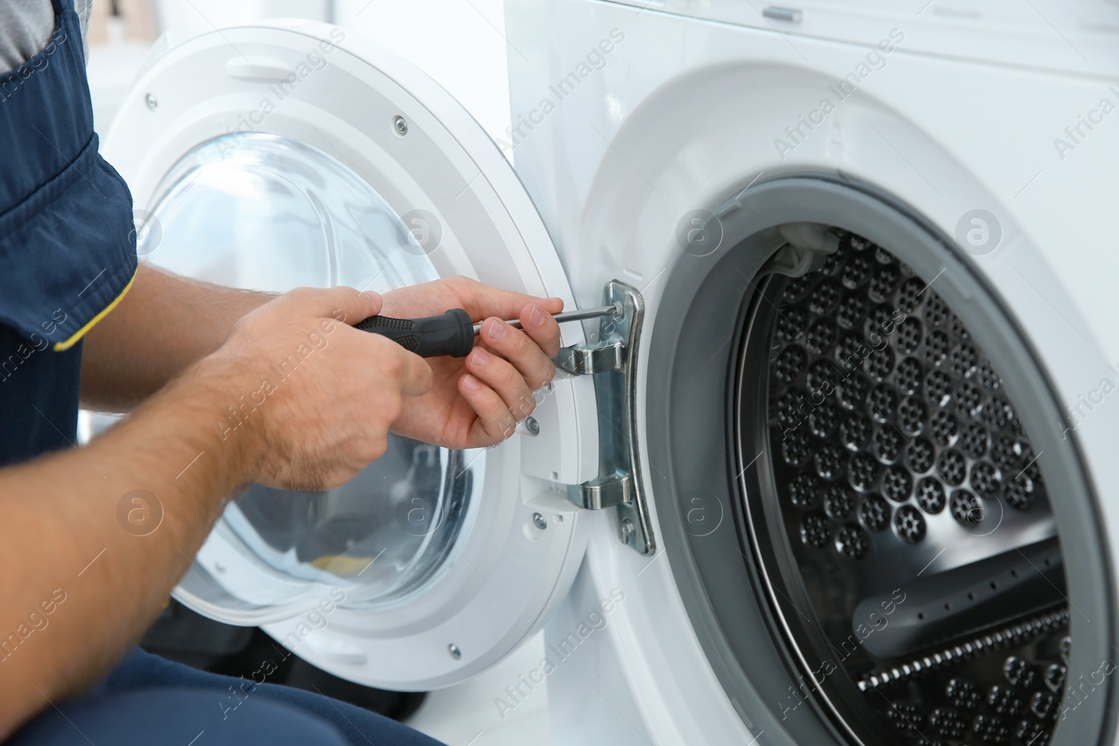 Photo of Young plumber fixing washing machine in bathroom, closeup