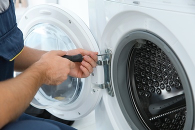 Young plumber fixing washing machine in bathroom, closeup