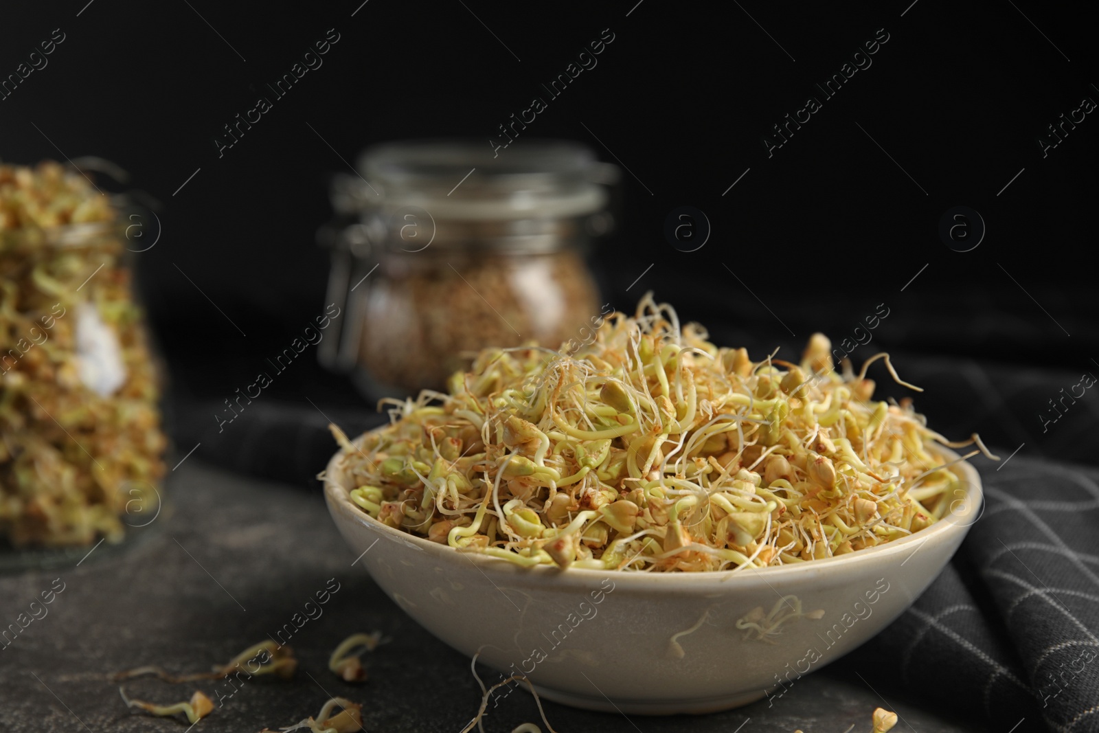 Photo of Bowl of sprouted green buckwheat on grey table, closeup