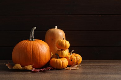 Photo of Thanksgiving day. Pumpkins and leaves on wooden table, space for text