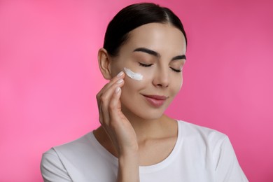 Photo of Young woman applying facial cream on pink background