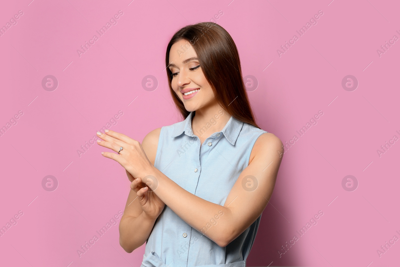 Photo of Happy young woman wearing beautiful engagement ring on pink background