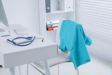 Photo of Turquoise medical uniform hanging on chair in clinic
