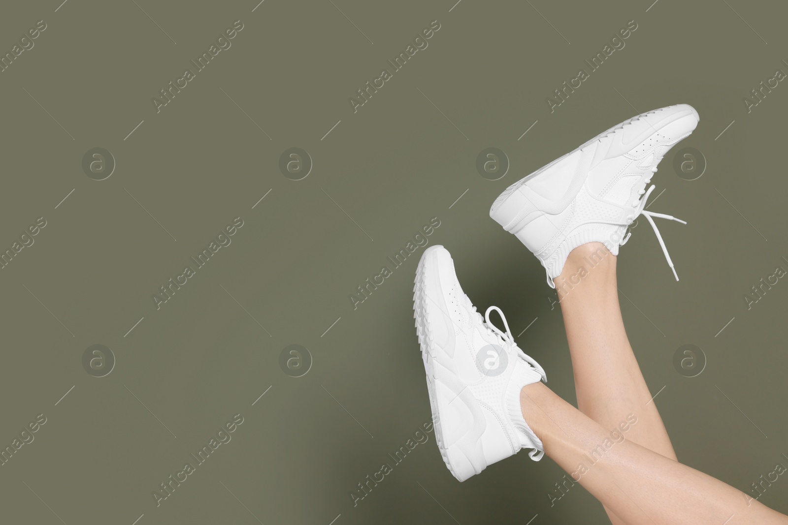 Photo of Woman wearing pair of new stylish sneakers on dark olive background, closeup. Space for text