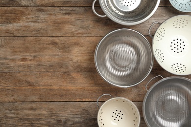 Many different colanders on wooden table, flat lay with space for text. Cooking utensils