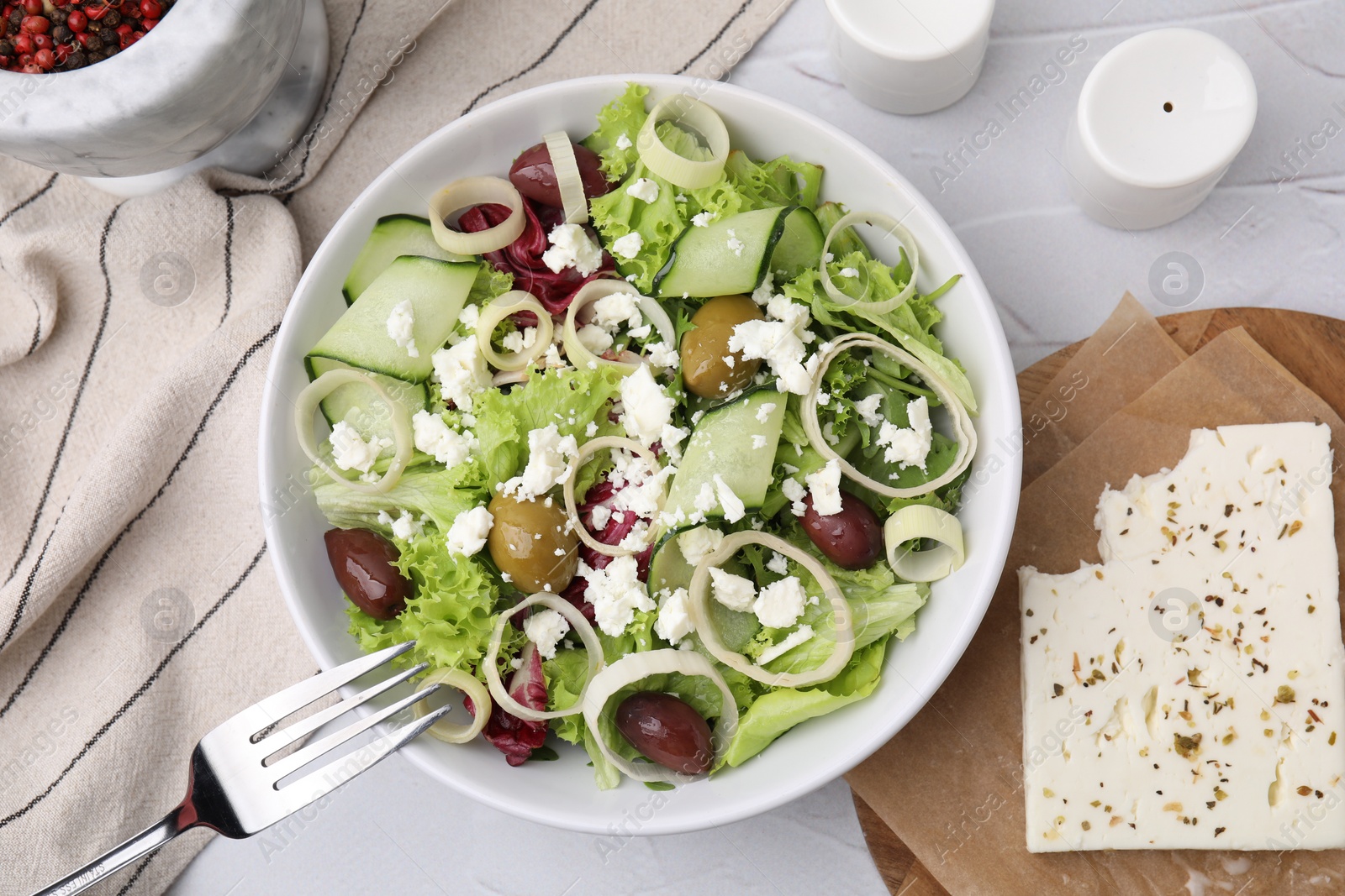 Photo of Bowl of tasty salad with leek, olives and cheese on white textured table, flat lay