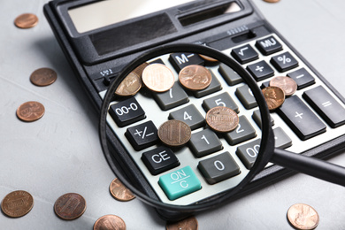 Looking through magnifying glass at calculator with coins on light grey table, closeup. Search concept