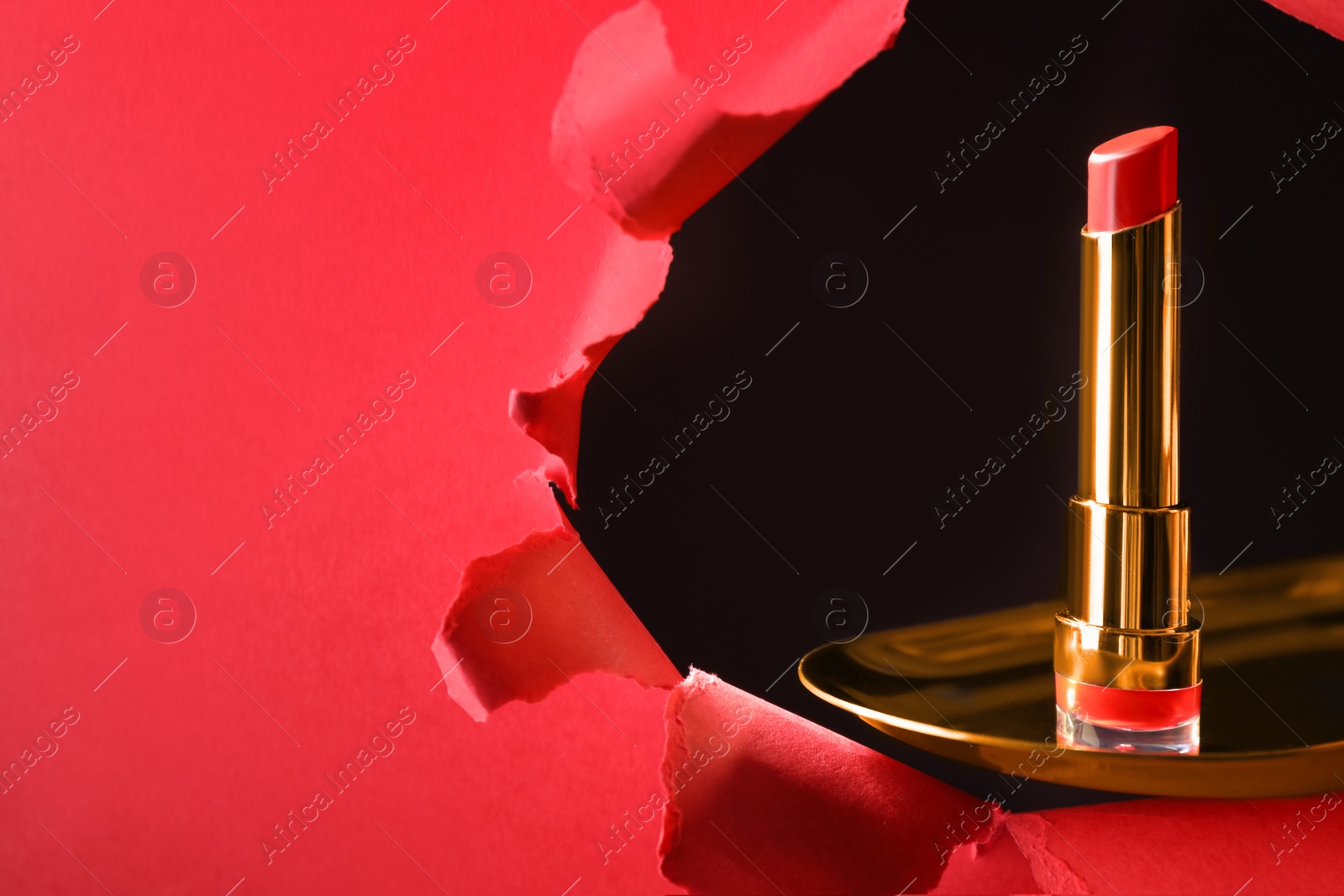 Photo of Bright red lipstick on gold plate, view through hole in paper