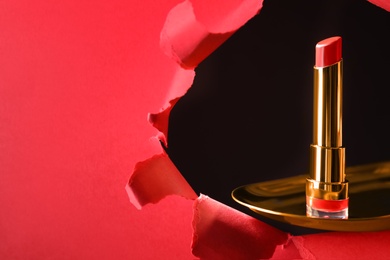 Photo of Bright red lipstick on gold plate, view through hole in paper