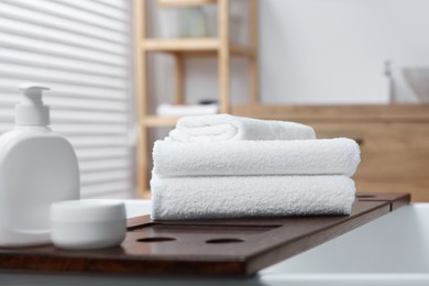Photo of Stacked bath towels and personal care products on tub tray in bathroom