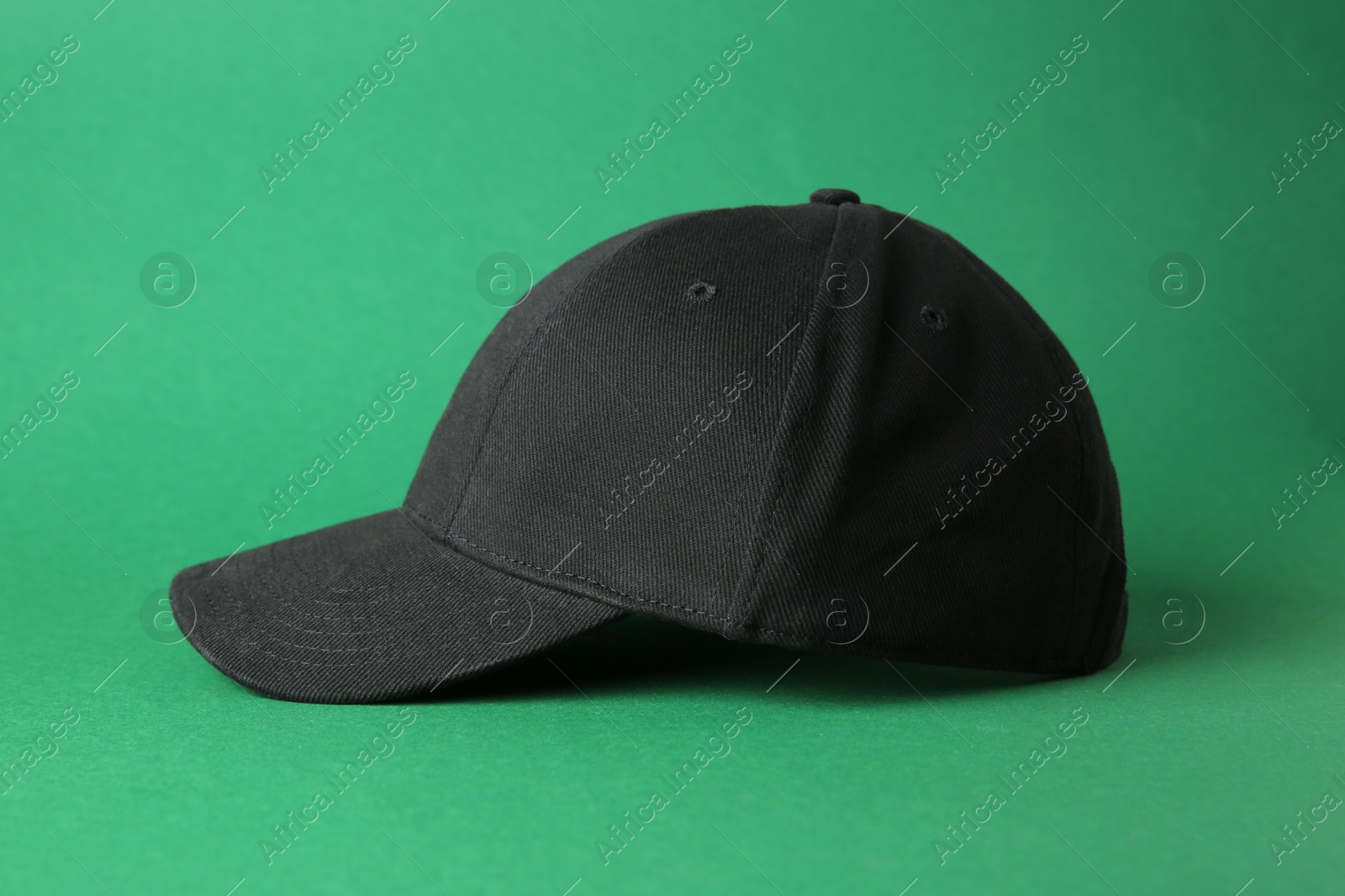 Photo of Stylish black baseball cap on green background