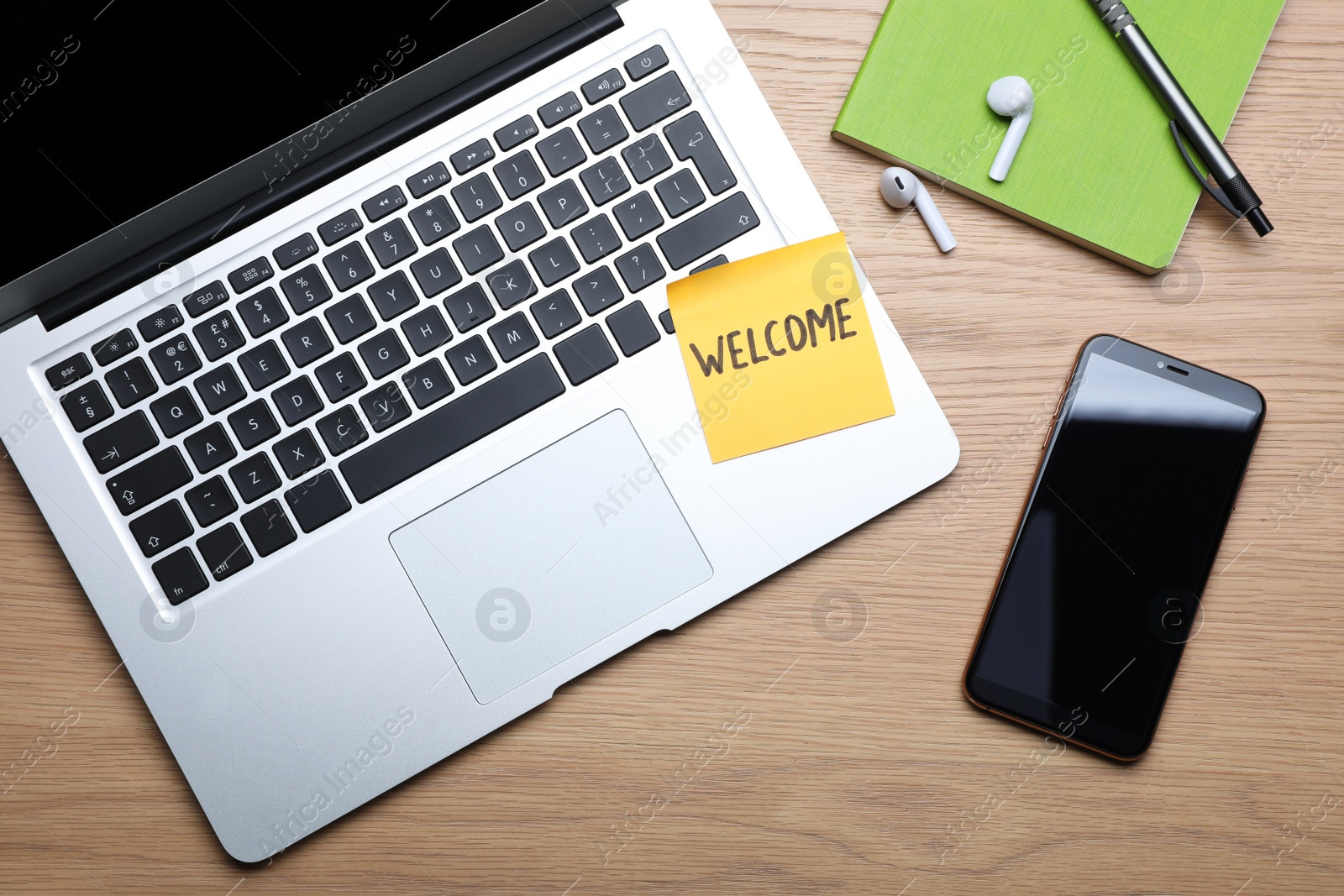 Photo of Paper note with word WELCOME, laptop and smartphone at workplace, flat lay