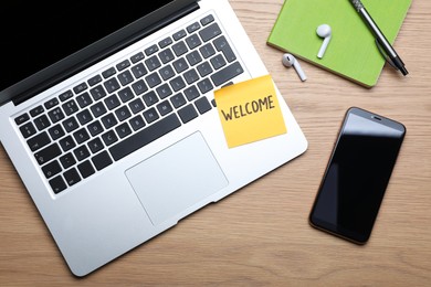 Paper note with word WELCOME, laptop and smartphone at workplace, flat lay