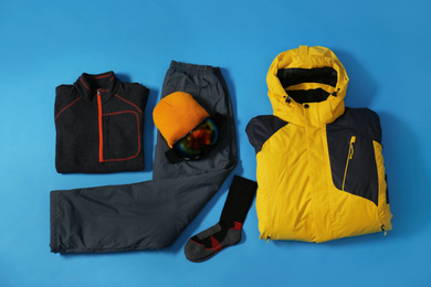 Stylish winter sport clothes on light blue background, flat lay