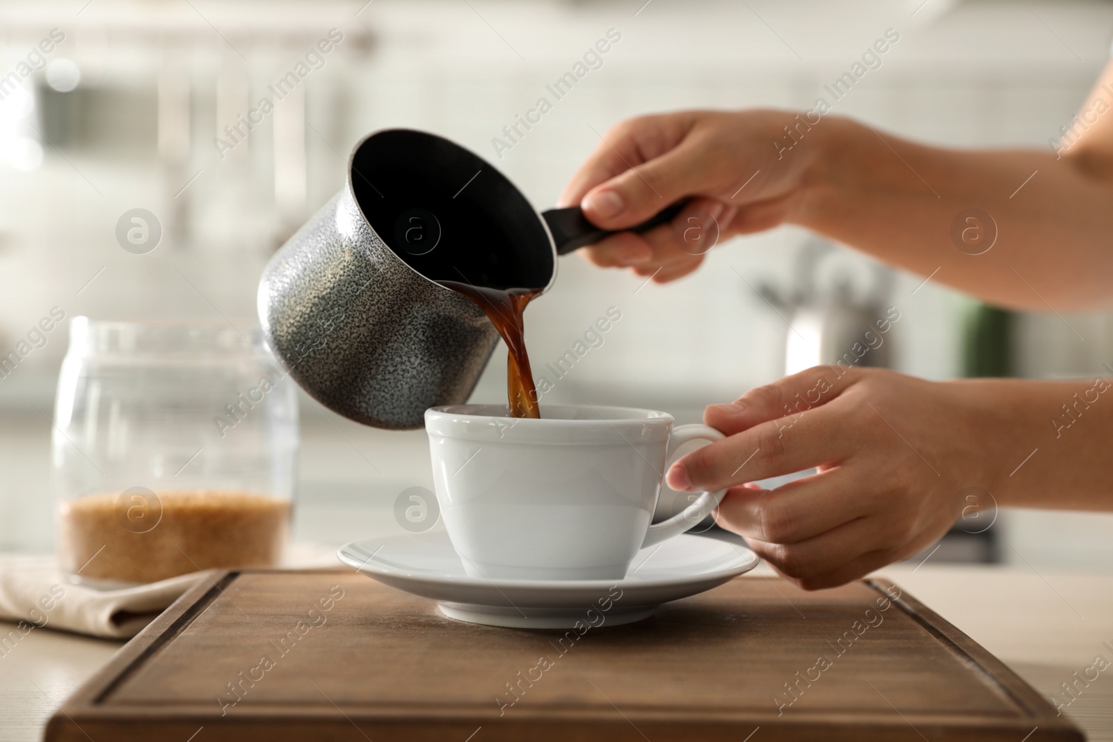 Photo of Woman pouring fresh coffee into cup at table in kitchen, closeup