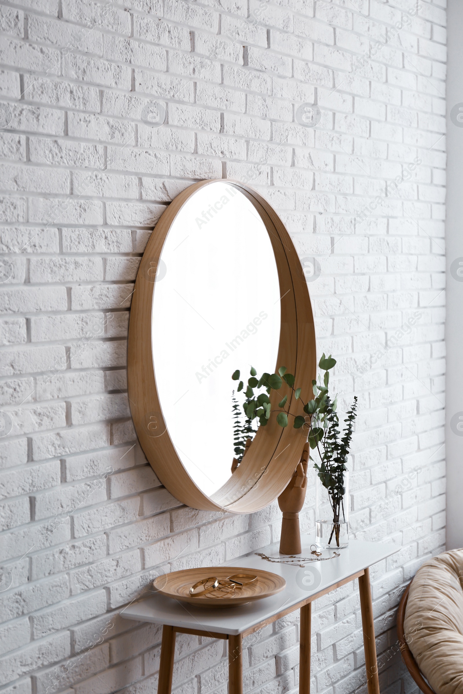 Photo of Big round mirror, table with jewelry and decor near brick wall in hallway interior