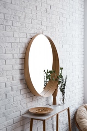 Photo of Big round mirror, table with jewelry and decor near brick wall in hallway interior