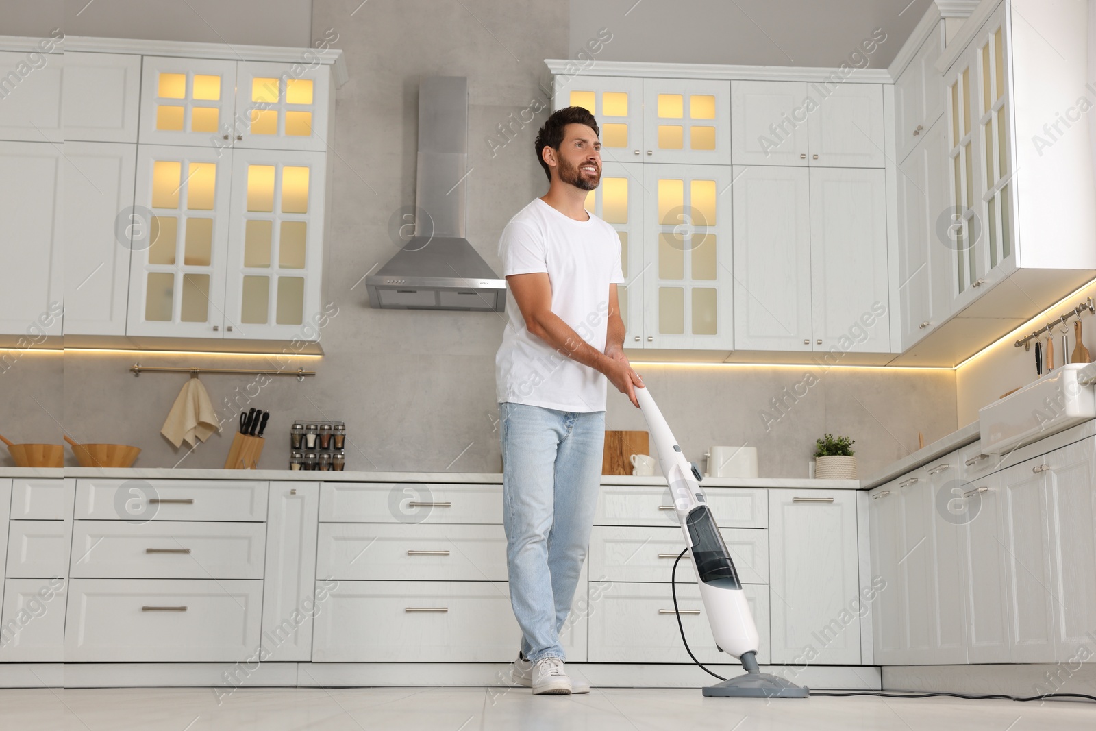 Photo of Happy man cleaning floor with steam mop in kitchen at home, low angle view