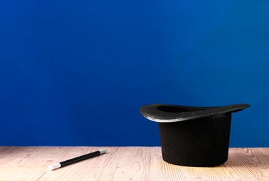 Photo of Magician's hat and wand on wooden table against blue background, space for text