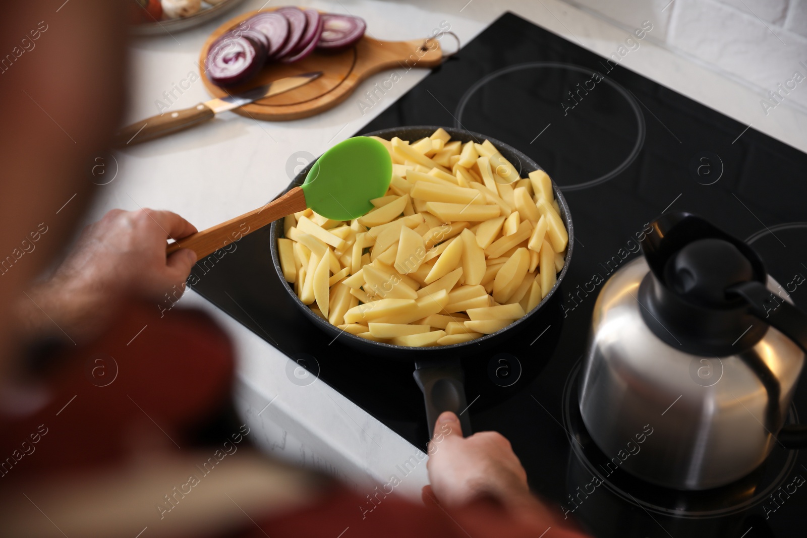 Photo of Man stirring cut raw potatoes in frying pan, closeup