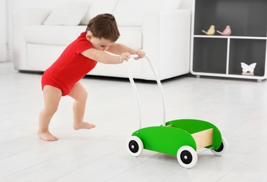 Cute baby playing with toy walker at home